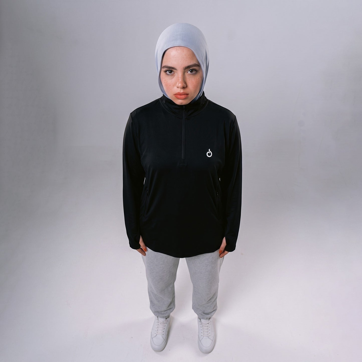 Model wearing Meryia WASEA’ black half-zip top with light grey hijab, grey joggers, and white sneakers.