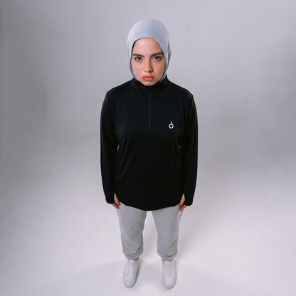 Model wearing Meryia WASEA’ black half-zip top with light grey hijab, grey joggers, and white sneakers. | Meryia مِرية