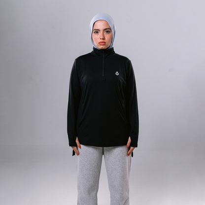 Meryia WASEA’ Zip Top in black with a half-zip neckline, worn by a model in a light blue hijab and grey joggers. | Meryia مِرية