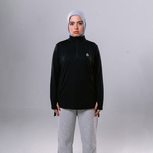 Meryia WASEA’ Zip Top in black with a half-zip neckline, worn by a model in a light blue hijab and grey joggers. | Meryia مِرية