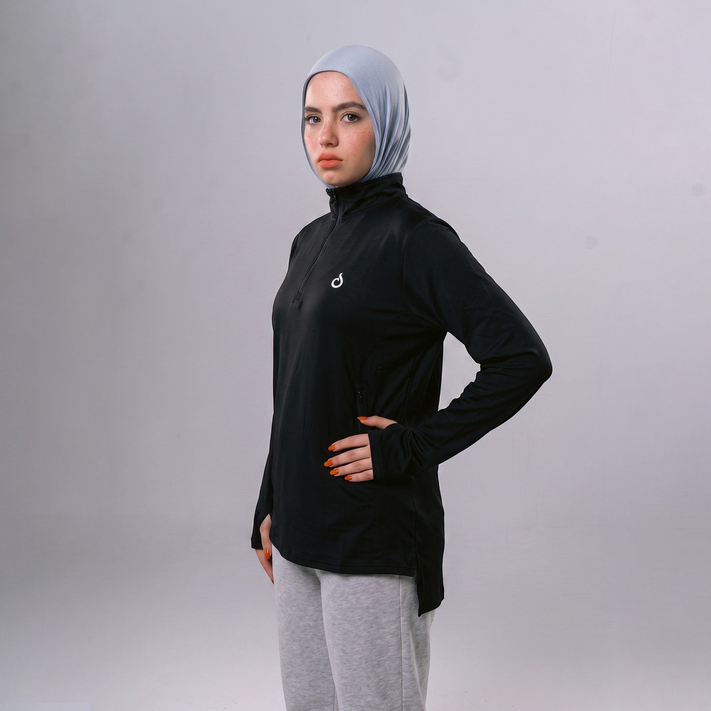 Meryia WASEA Zip Top in black with half-zip neckline, worn by a model in a light blue hijab and grey joggers.